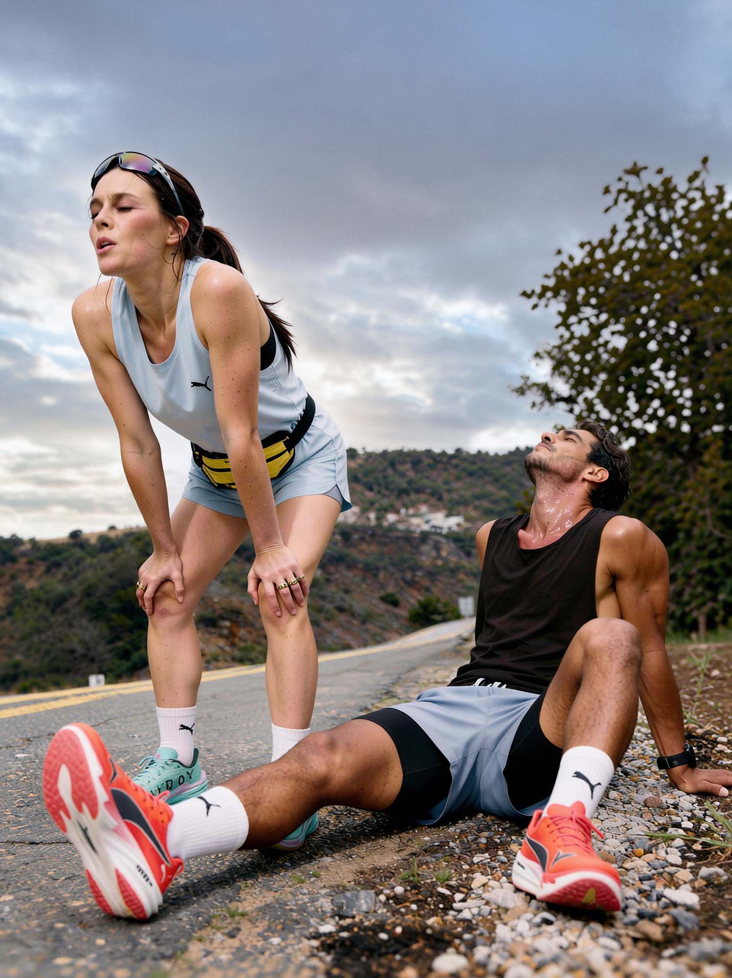 A man and a woman after finishing a hard long run on a quiet rural road, caught in the moment after honest exertion, not posing. The man and woman are in a recovery position.