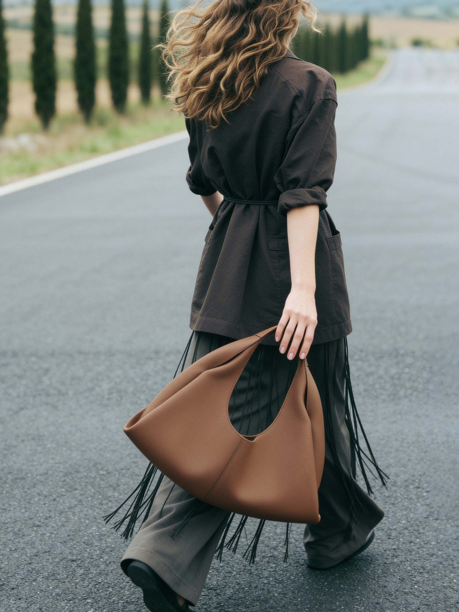 A woman walks across a piazza in a southern Italian town in soft, even morning light, seen from a slight side angle, mid-stride, carrying a large burgundy pebbled-leather tote over her right shoulder